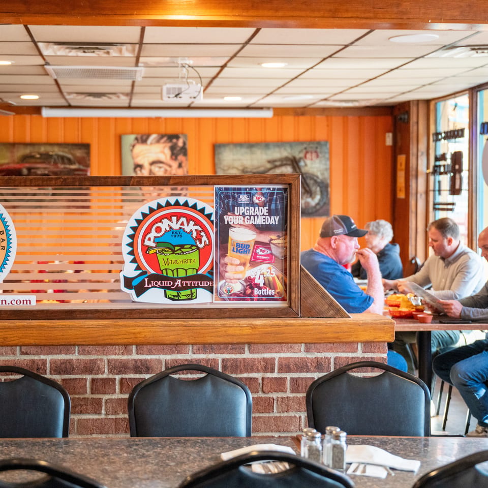 Ponak’s Mexican restaurant dining room with colorful logos, wood-paneled walls, and diners eating at tables near windows.