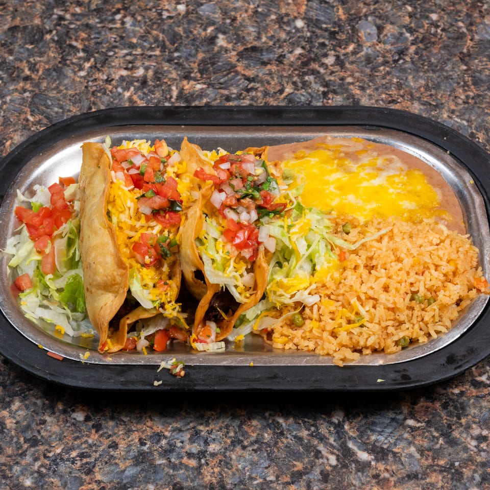 Three crispy tacos topped with lettuce, cheese, and pico de gallo served with refried beans and Mexican rice on a platter.