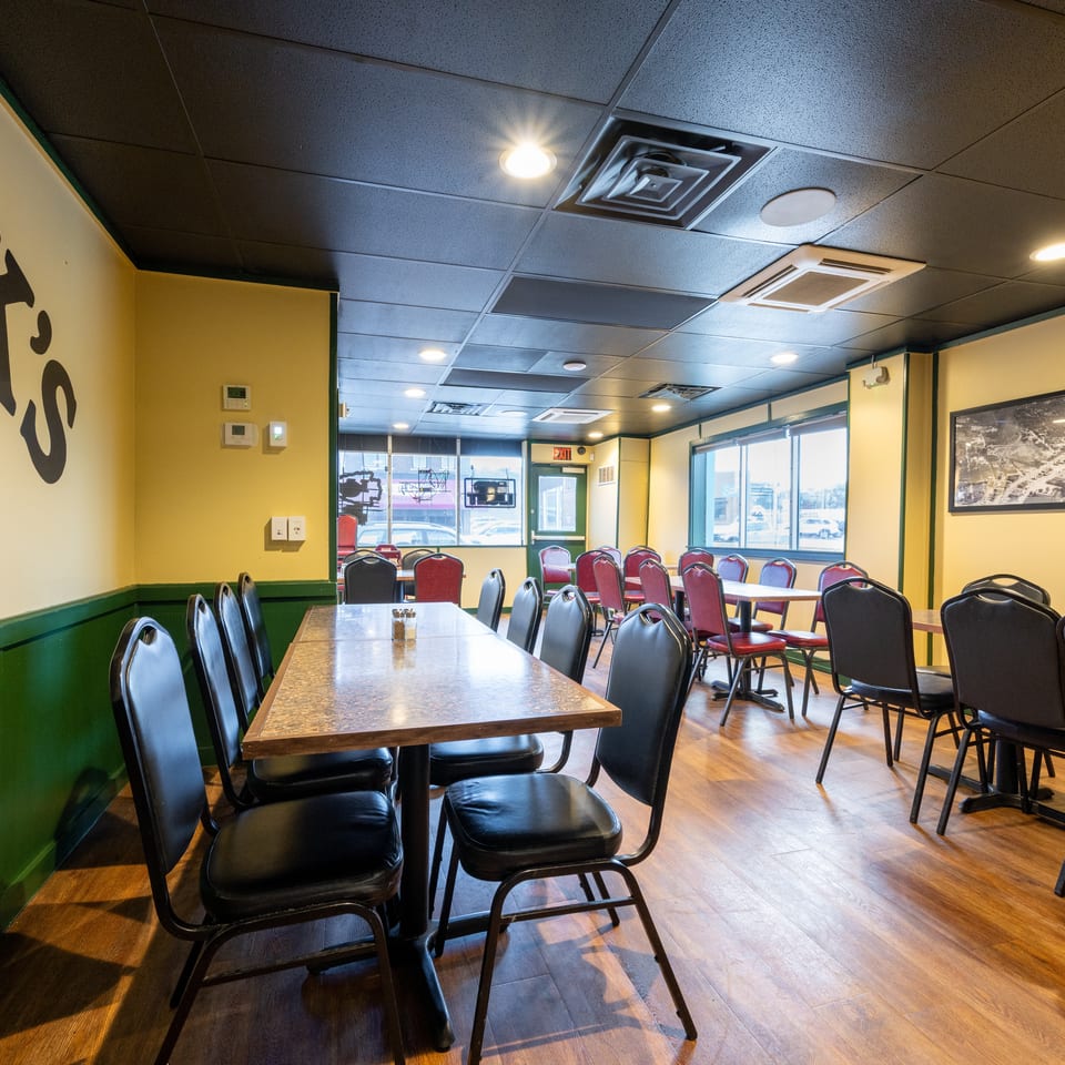 Bright casual restaurant dining room with yellow and green walls, wood floors, and rows of tables surrounded by black and red chairs.
