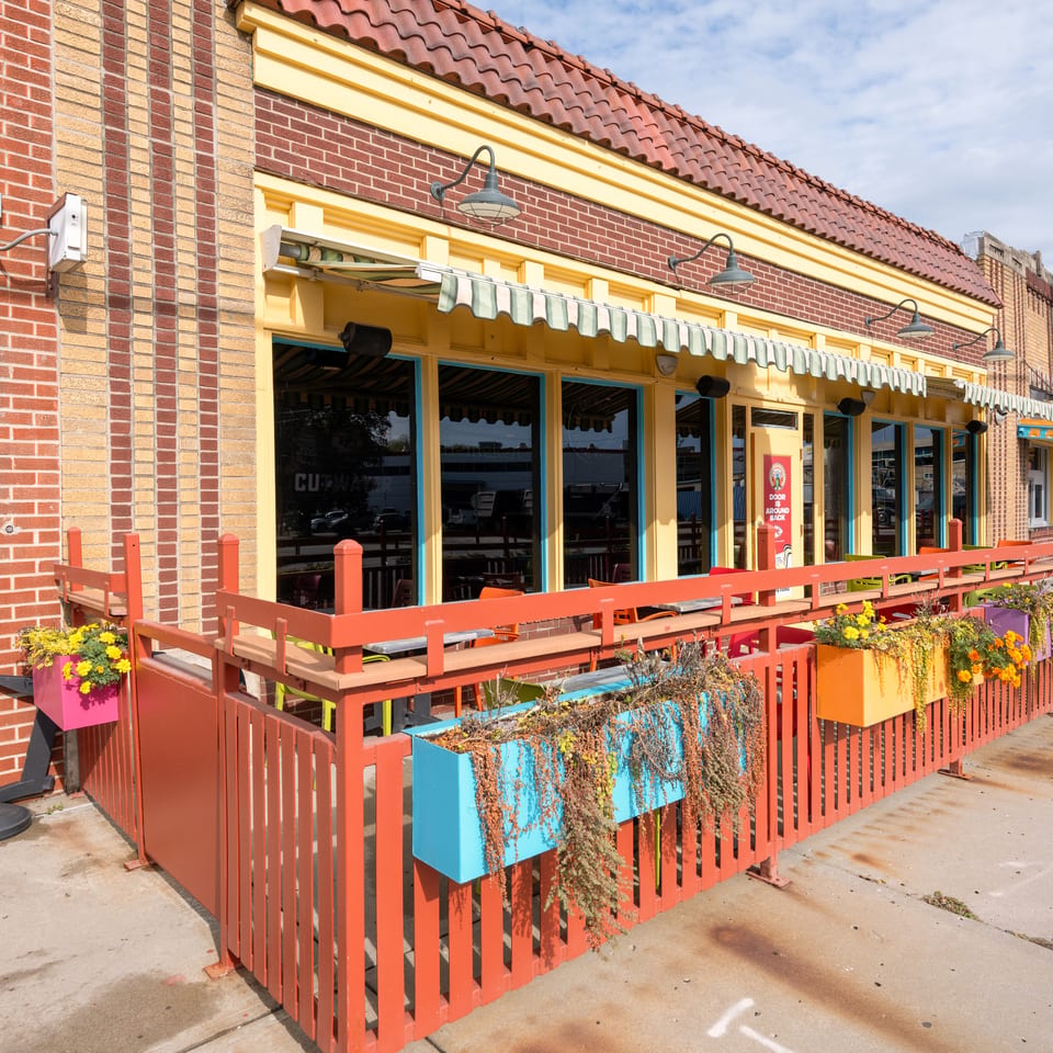 Colorful Ponak’s restaurant storefront with red brick walls, striped awning, outdoor patio seating, and flower-filled planters.