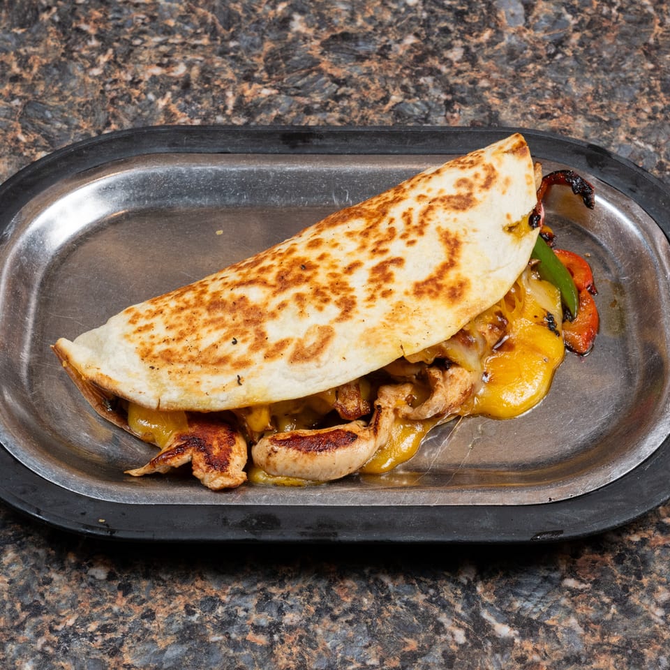 Grilled chicken quesadilla with melted cheese and sautéed peppers on a black metal tray.