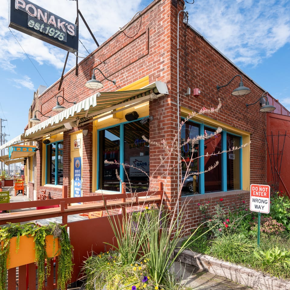 Exterior of Ponder’s brick restaurant with colorful trim, outdoor patio seating, hanging sign, and landscaped entrance.