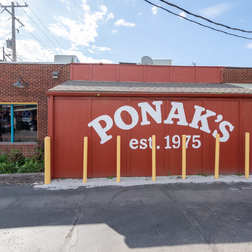 Exterior of Ponak’s restaurant featuring a red brick building, large painted sign, yellow bollards, and sunny blue sky.