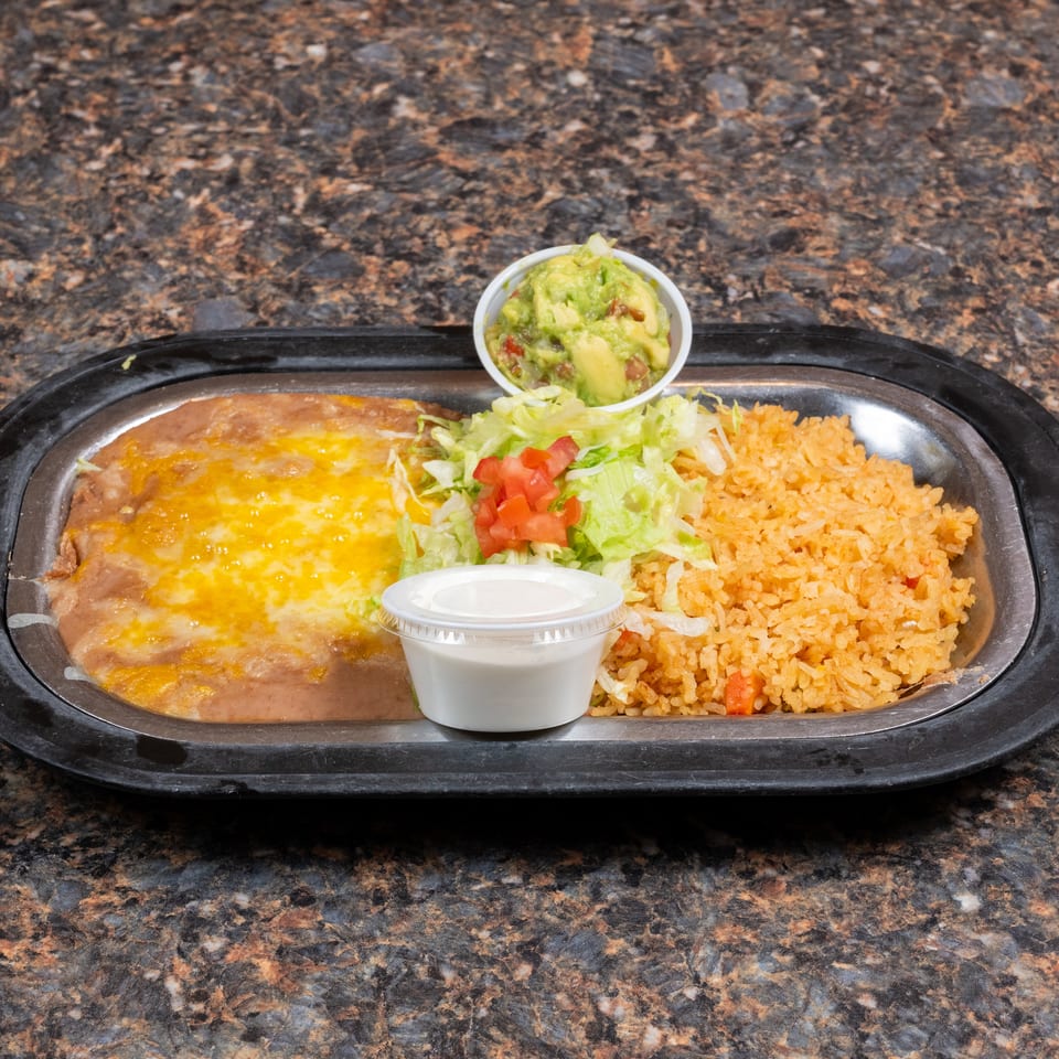 Mexican meal with cheese-topped refried beans, seasoned rice, lettuce salad, guacamole, and sour cream on a black tray.